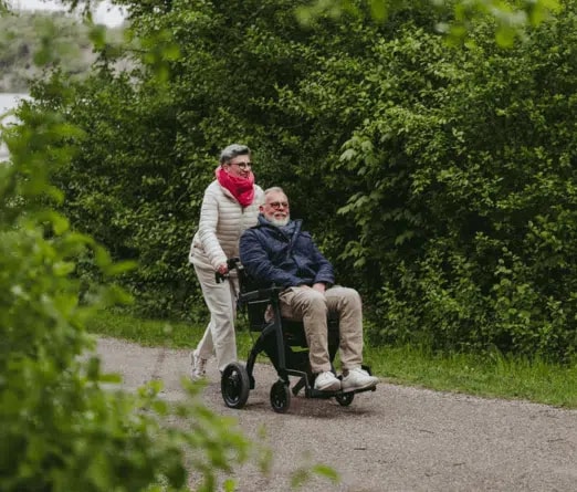 Een vrouw duwt een man in de Rollz Motion Electric over een bospad