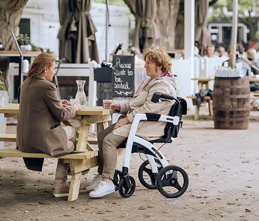 Twee vriendinnen op een terras, een van hen zit in de Rollz Motion als rolstoel