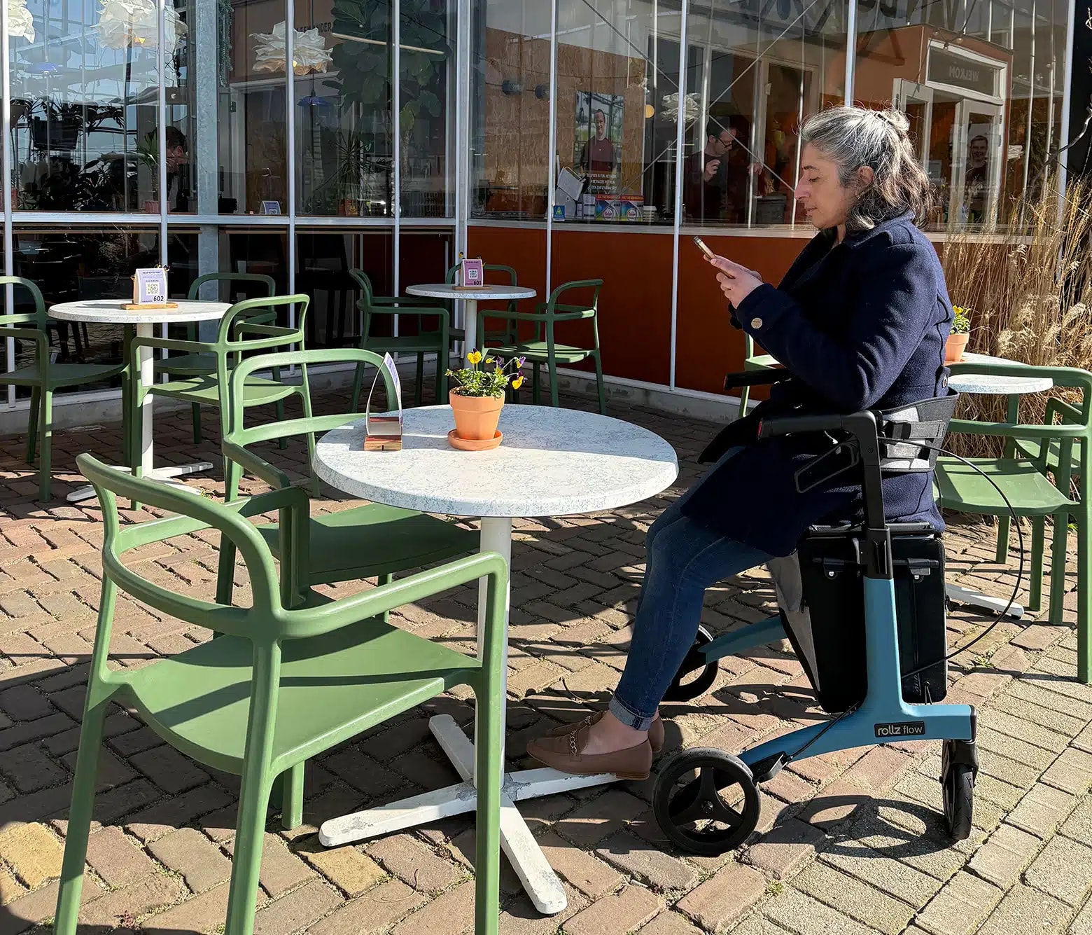 Een vrouw zit op het zitje van de Rollz Flow aan een terrastafel