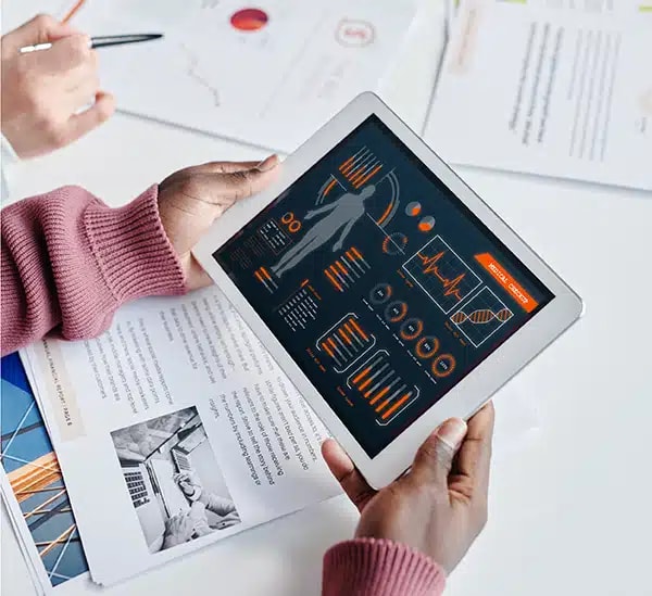 Handen houden een tablet met medische gegevens boven papieren rapporten.