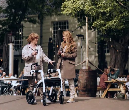Twee vrouwen staan met een koffie te praten op een terras, de oudste met haar witte Rollz Motion.