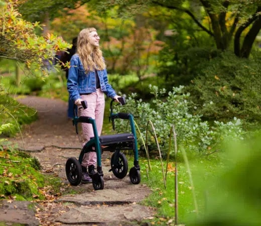 Een jonge vrouw in een spijkerjack loopt met de groene Rollz Motion Performance over een stenen pad in een tuin.