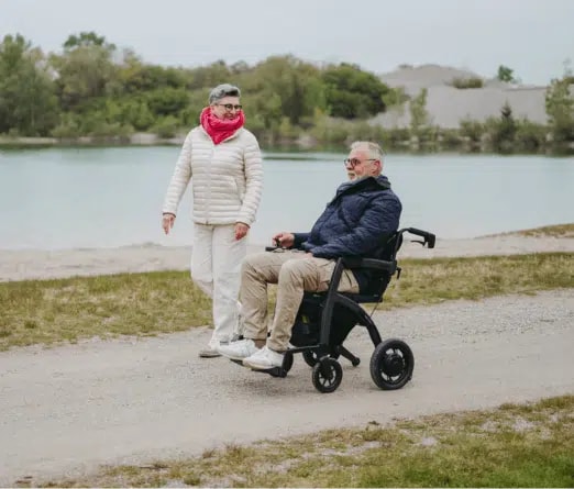 Een man rijdt in zijn zwarte Rollz Motion Electric over een pad langs het water, een vrouw met een rode sjaal loopt naast hem.