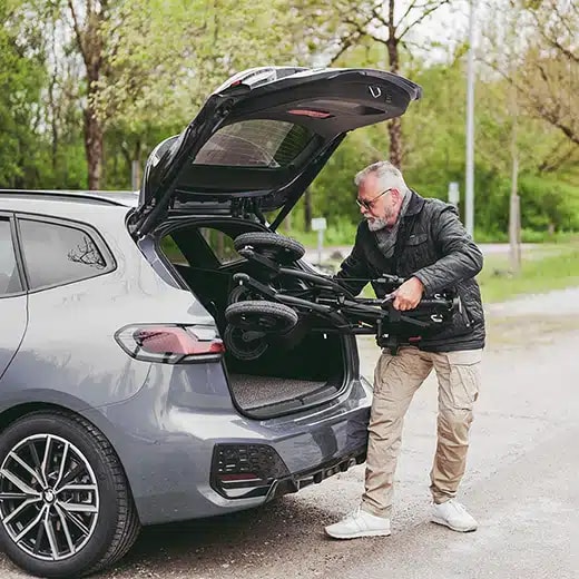 Een man tilt de opgevouwen Rollz Motion Electric in de kofferbak van zijn auto.