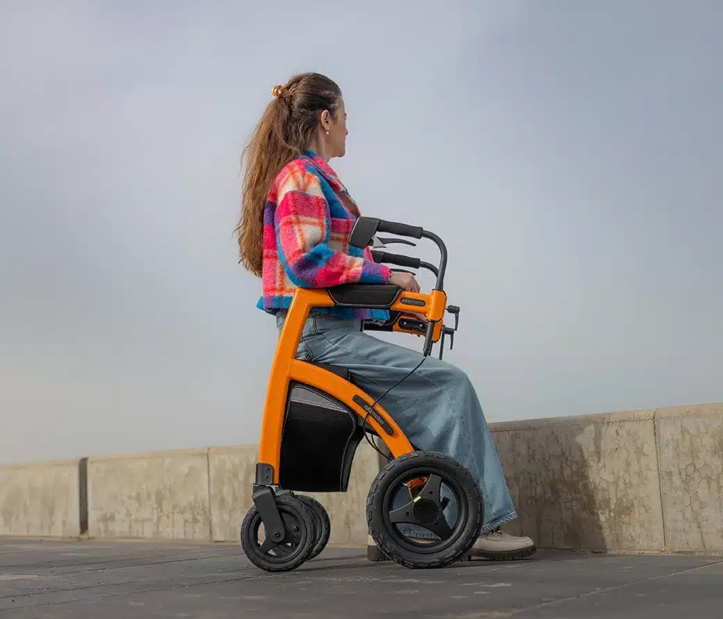 Een vrouw zit op de oranje Rollz Motion Performance in rolstoelstand op een kade aan zee.